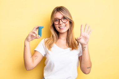 Güzel sarışın kız gülümsüyor ve arkadaş canlısı görünüyor, dört numarayı gösteriyor. astım spreyi kavramı