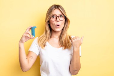 Güzel sarışın kız inançsızlıktan şaşkın şaşkın bakıyor. astım spreyi kavramı