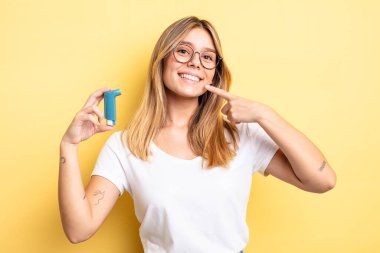 Güzel sarışın kız kendi gülüşünü göstererek kendine güvenerek gülümsüyor. astım spreyi kavramı