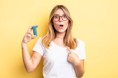 Şok olmuş ve ağzı açık, kendini işaret eden güzel sarışın bir kız. astım spreyi kavramı