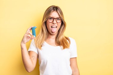 Güzel sarışın kız iğreniyor, sinirleniyor ve dilini çıkarıyor. astım spreyi kavramı