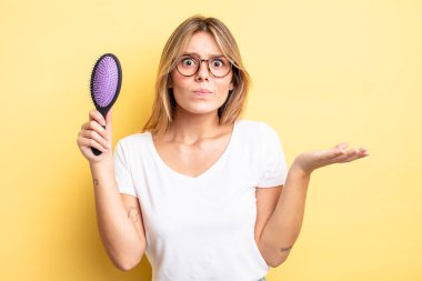 Güzel sarışın kız şaşkın, şaşkın ve şüpheci hissediyor. saç fırçası konsepti