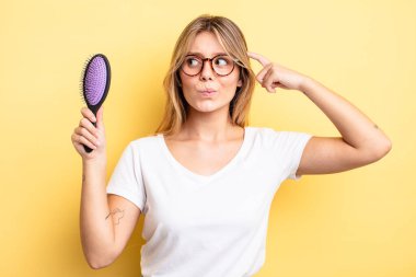 Güzel sarışın kız mutlu bir şekilde gülümsüyor ve hayal kuruyor ya da şüphe ediyor. saç fırçası konsepti