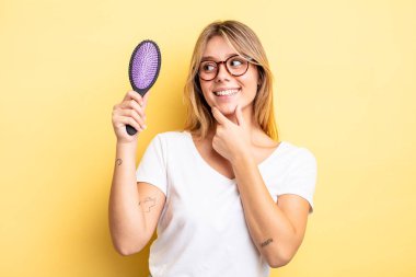 Güzel sarışın kız gülümsüyor mutlu, kendine güvenen bir yüz ifadesi ve elleri çenesinde. saç fırçası konsepti