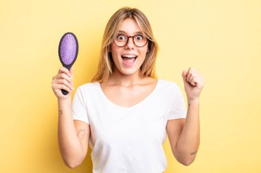 Güzel sarışın kız şokta, gülüyor ve başarıyı kutluyor. saç fırçası konsepti