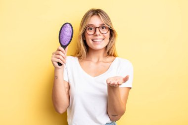 Güzel sarışın kız mutlu bir şekilde gülümsüyor ve bir konsept sunuyor. saç fırçası konsepti