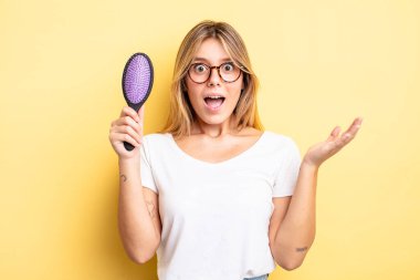 Güzel sarışın kız kendini mutlu hissediyor ve inanılmaz bir şeye hayret ediyor. saç fırçası konsepti