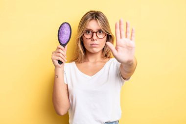 Güzel sarışın kız ciddi görünüyor. Avuç içini gösteriyor. Durma hareketi yapıyor. saç fırçası konsepti