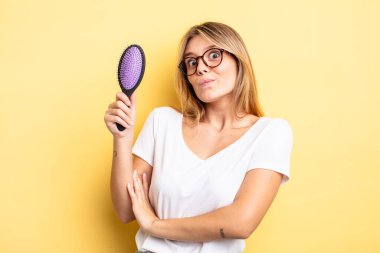 Güzel sarışın kız omuz silkiyor, kafası karışık ve kararsız. saç fırçası konsepti