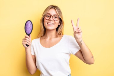 Güzel sarışın kız gülümsüyor ve arkadaş canlısı görünüyor. İki numarayı gösteriyor. saç fırçası konsepti