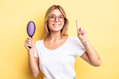 Güzel sarışın kız gülümsüyor ve arkadaş canlısı görünüyor. Bir numarayı gösteriyor. saç fırçası konsepti