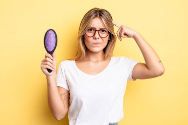 Güzel sarışın kız şaşkın ve şaşkın hissediyor, senin deli olduğunu gösteriyor. saç fırçası konsepti