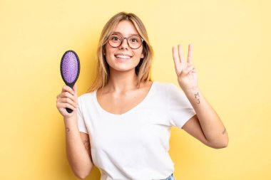 Güzel sarışın kız gülümsüyor ve arkadaş canlısı görünüyor, üç numarayı gösteriyor. saç fırçası konsepti