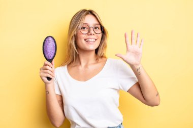 Güzel sarışın kız gülümsüyor ve arkadaş canlısı görünüyor, beş numarayı gösteriyor. saç fırçası konsepti