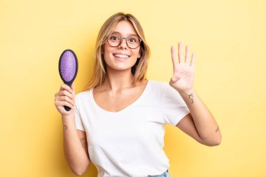 Güzel sarışın kız gülümsüyor ve arkadaş canlısı görünüyor, dört numarayı gösteriyor. saç fırçası konsepti