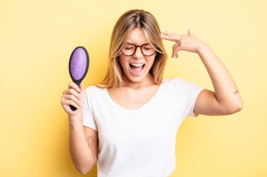 Güzel sarışın kız mutsuz ve stresli görünüyor, intihar jesti silah işareti yapıyor. saç fırçası konsepti