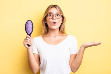 Güzel sarışın kız şaşırmış ve şok olmuş görünüyor. Çenesi düşmüş ve elinde bir nesne var. saç fırçası konsepti