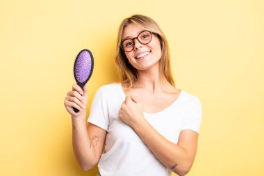 Güzel sarışın kız kendini mutlu hissediyor ve bir meydan okumayla yüzleşiyor ya da kutluyor. saç fırçası konsepti