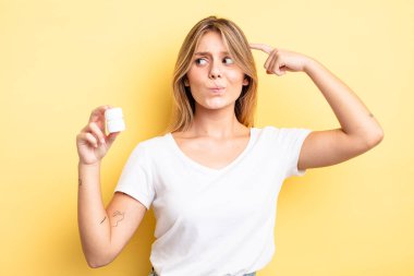 Güzel sarışın kız şaşkın ve kafası karışık, kaşınan bir kafa hissediyor. hap şişesi konsepti