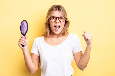 Güzel sarışın kız sinirli bir ifadeyle agresif bir şekilde bağırıyor. saç fırçası konsepti