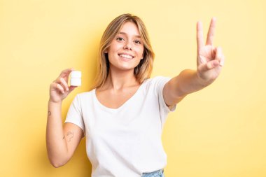 Güzel sarışın kız gülümsüyor ve mutlu görünüyor, zafer ya da barış işareti yapıyor. hap şişesi konsepti