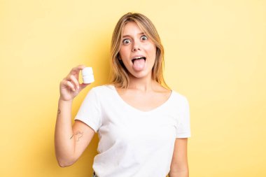 Güzel sarışın, neşeli ve asi tavırlı, şaka yapan ve dilini dışarı çıkaran bir kız. hap şişesi konsepti