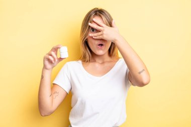 Güzel sarışın kız şok olmuş, korkmuş ya da korkmuş görünüyor. Yüzü elle kapatılmış. hap şişesi konsepti