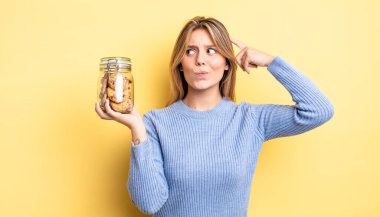 Güzel sarışın kız şaşkın ve kafası karışık, kaşınan bir kafa hissediyor. Ev yapımı kurabiye konsepti