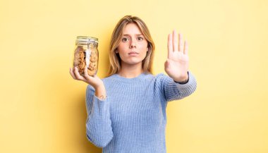 Güzel sarışın kız ciddi görünüyor. Avuç içini gösteriyor. Durma hareketi yapıyor. Ev yapımı kurabiye konsepti