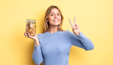 Güzel sarışın kız gülümsüyor ve arkadaş canlısı görünüyor. İki numarayı gösteriyor. Ev yapımı kurabiye konsepti