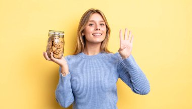 Güzel sarışın kız gülümsüyor ve arkadaş canlısı görünüyor, dört numarayı gösteriyor. Ev yapımı kurabiye konsepti
