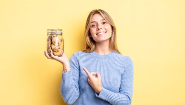 Güzel sarışın kız neşeyle gülümsüyor, mutlu hissediyor ve bir tarafı işaret ediyor. Ev yapımı kurabiye konsepti