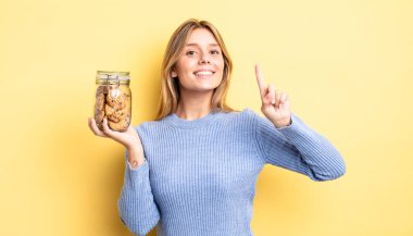 Güzel sarışın kız gülümsüyor ve arkadaş canlısı görünüyor. Bir numarayı gösteriyor. Ev yapımı kurabiye konsepti