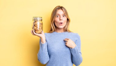 Şok olmuş ve ağzı açık, kendini işaret eden güzel sarışın bir kız. Ev yapımı kurabiye konsepti