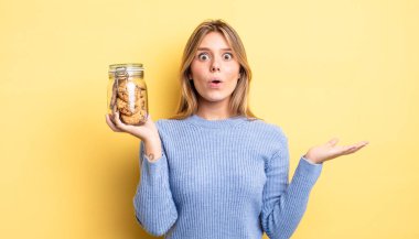 Güzel sarışın kız şaşırmış ve şok olmuş görünüyor. Çenesi düşmüş ve elinde bir nesne var. Ev yapımı kurabiye konsepti