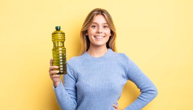 Güzel sarışın kız mutlu bir şekilde gülümsüyor, eli kalçasında ve kendinden emin. Zeytin yağı kavramı