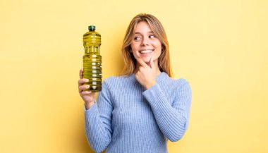 Güzel sarışın kız gülümsüyor mutlu, kendine güvenen bir yüz ifadesi ve elleri çenesinde. Zeytin yağı kavramı
