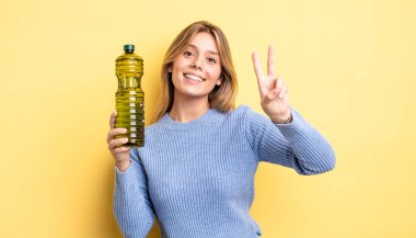 Güzel sarışın kız gülümsüyor ve mutlu görünüyor, zafer ya da barış işareti yapıyor. Zeytin yağı kavramı