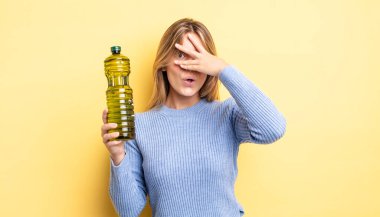 Güzel sarışın kız şok olmuş, korkmuş ya da korkmuş görünüyor. Yüzü elle kapatılmış. Zeytin yağı kavramı