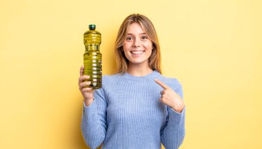 Güzel sarışın kız mutlu hissediyor ve heyecanla kendini işaret ediyor. Zeytin yağı kavramı