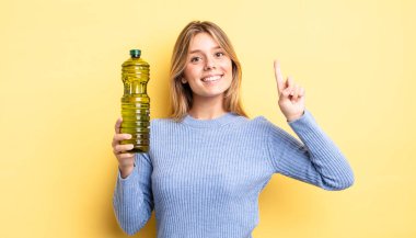 Güzel sarışın kız gülümsüyor ve arkadaş canlısı görünüyor. Bir numarayı gösteriyor. Zeytin yağı kavramı