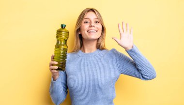 Güzel sarışın kız mutlu bir şekilde gülümsüyor, el sallıyor, hoş geldin diyor ve seni selamlıyor. Zeytin yağı kavramı