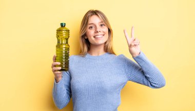 Güzel sarışın kız gülümsüyor ve arkadaş canlısı görünüyor. İki numarayı gösteriyor. Zeytin yağı kavramı