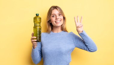 Güzel sarışın kız gülümsüyor ve arkadaş canlısı görünüyor, üç numarayı gösteriyor. Zeytin yağı kavramı