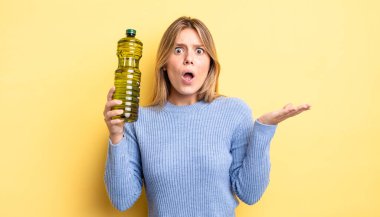 Güzel sarışın kız şaşırmış ve şok olmuş görünüyor. Çenesi düşmüş ve elinde bir nesne var. Zeytin yağı kavramı