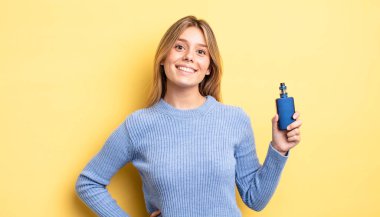 Güzel sarışın kız mutlu bir şekilde gülümsüyor, eli kalçasında ve kendinden emin. duman buharlaştırıcı kavramı