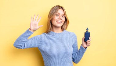 Güzel sarışın kız gülümsüyor ve arkadaş canlısı görünüyor, beş numarayı gösteriyor. duman buharlaştırıcı kavramı