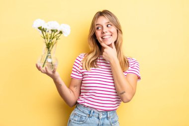 Güzel sarışın kız gülümsüyor mutlu, kendine güvenen bir yüz ifadesi ve elleri çenesinde. Dekoratif çiçek konsepti
