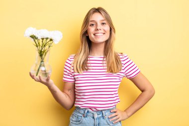 Güzel sarışın kız mutlu bir şekilde gülümsüyor, eli kalçasında ve kendinden emin. Dekoratif çiçek konsepti