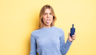 Güzel sarışın kız iğreniyor, sinirleniyor ve dilini çıkarıyor. duman buharlaştırıcı kavramı